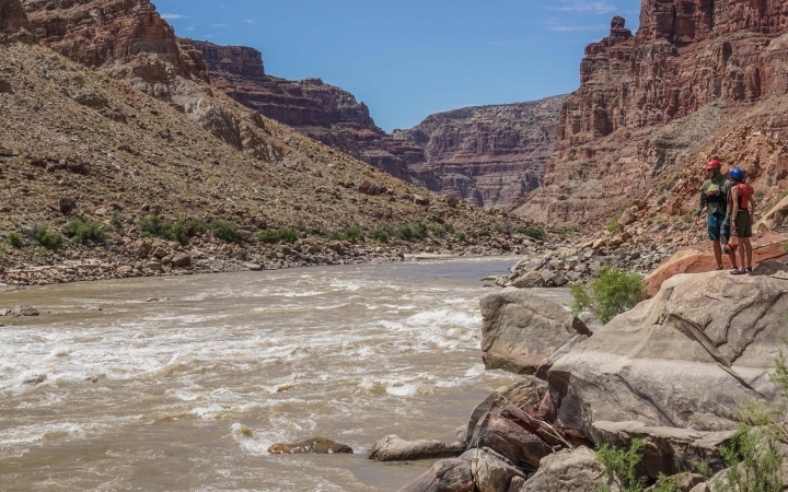 two people stand on a rock an survey a river flowing through a canyon